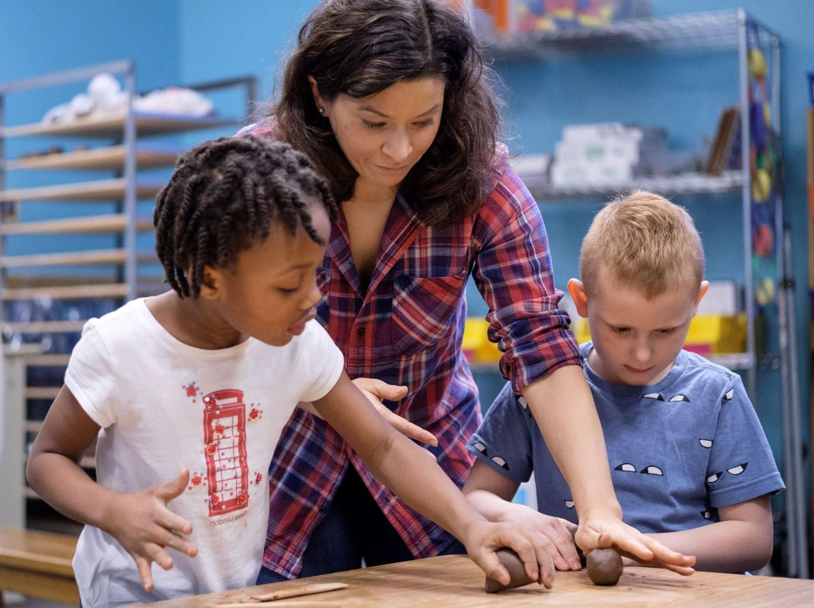 teacher working with two elementary students on a clay project