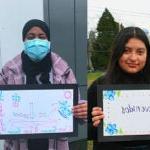 Several students stand with hand drawn signs that say welcome in many languages.