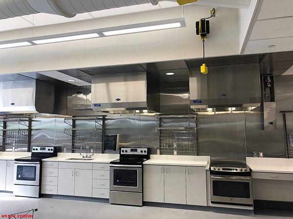 a large room with three stoves with counters between them and metal wall racks behind them
