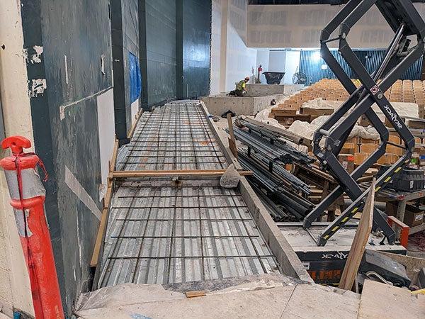 rebar in a wooden frame slopes up beside a wall. theater seats are next to the structure