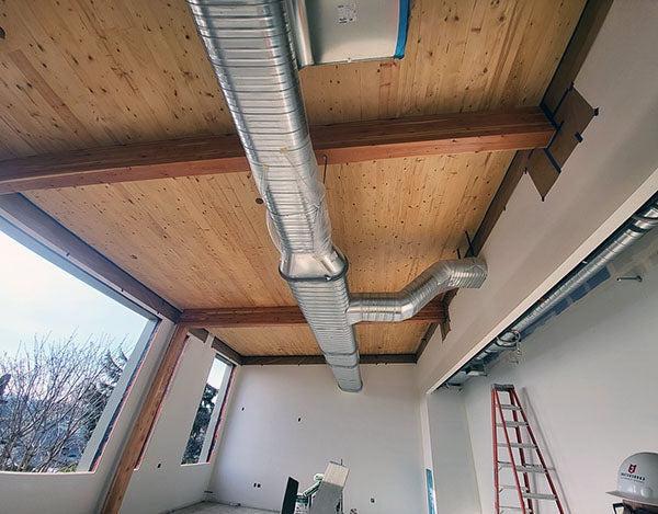 looking up toward a wood ceiling with a metal duct running across it. openings in the wall for windows are empty, wallboard is painted