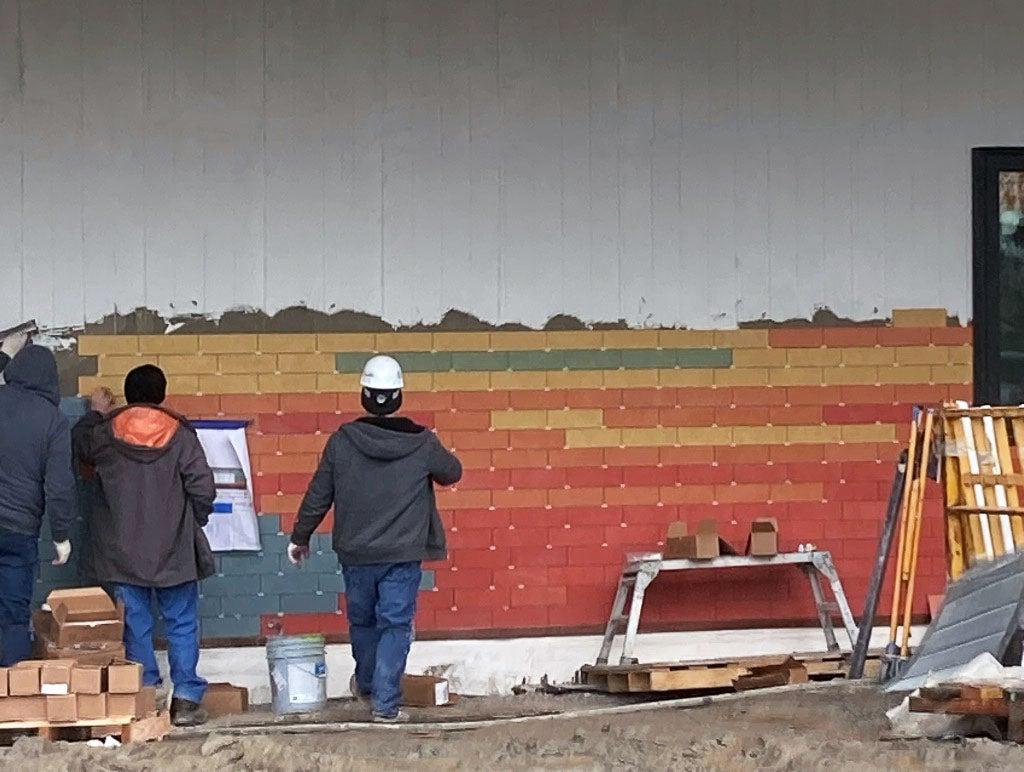 people are looking at brightly colored tiles on a wall. they wall is partly tiled, and partly prepped for tiles
