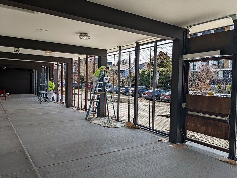 a covered walkway has workers on ladders while painting fence frames