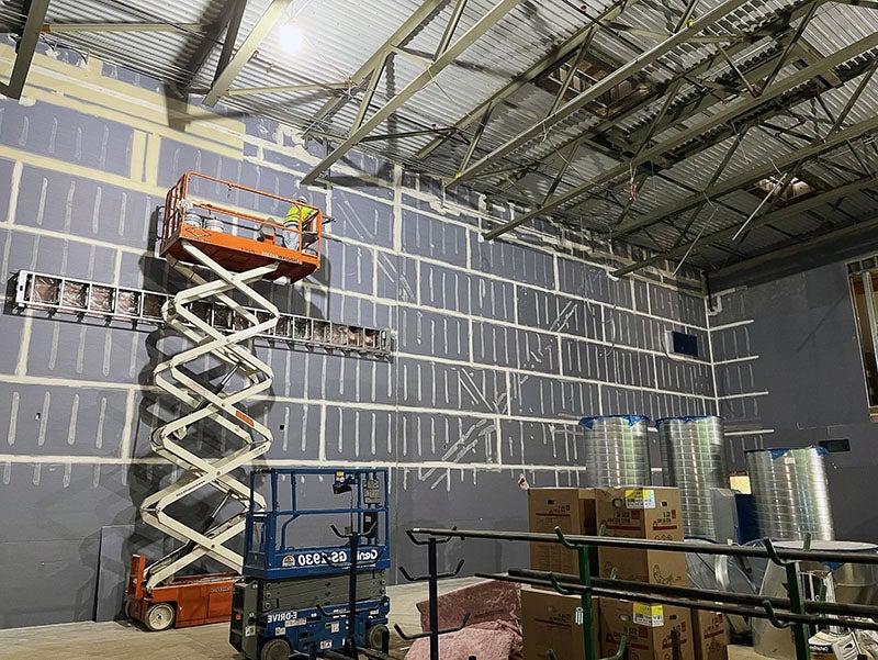 a worker on a scissor lift is taping wallboard in a two story room