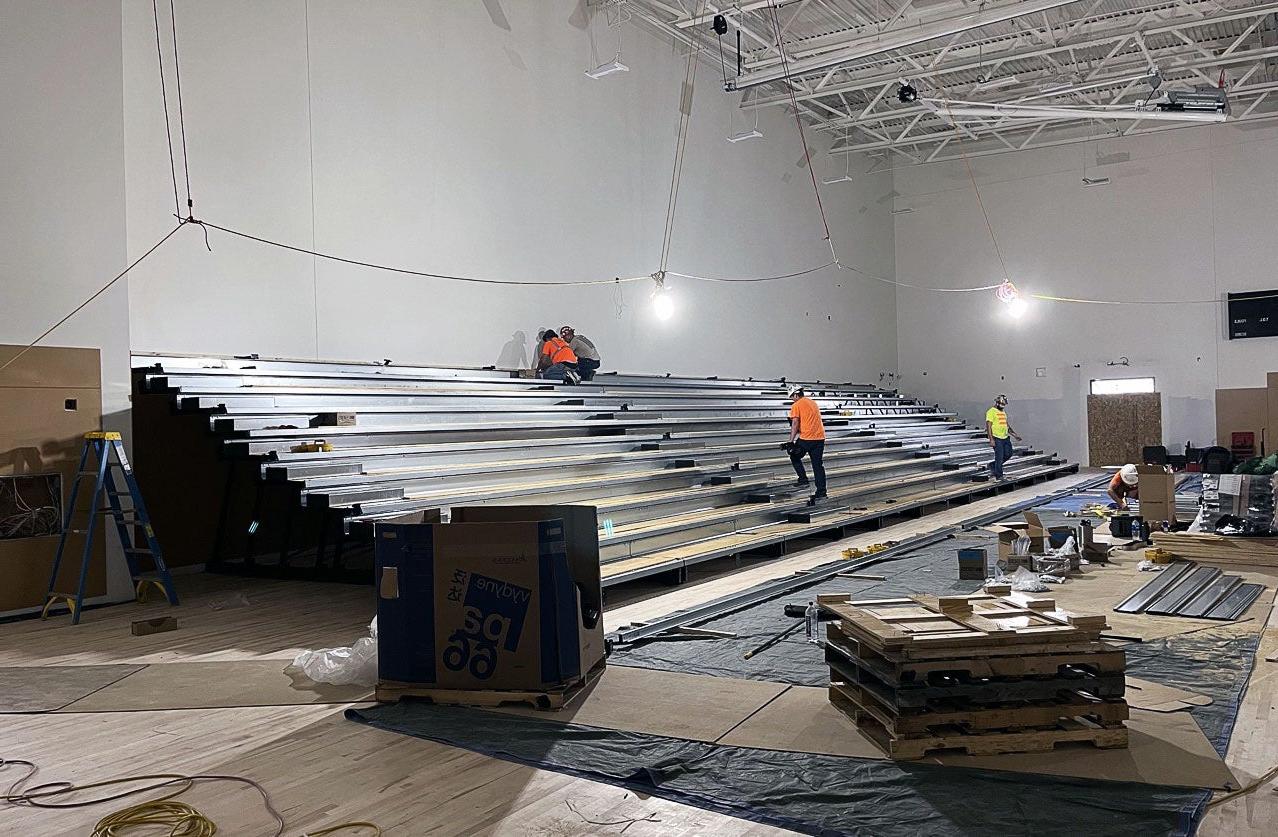 workers are installing bleachers in a large room with a high ceiling