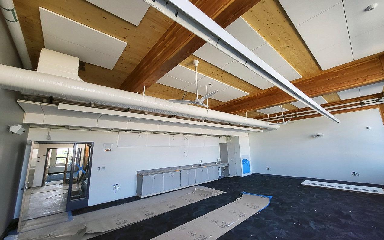 looking up toward the ceiling of a room that has glue lam beams and cross pieces of lighter colored wood - lighting fixtures are partially installed
