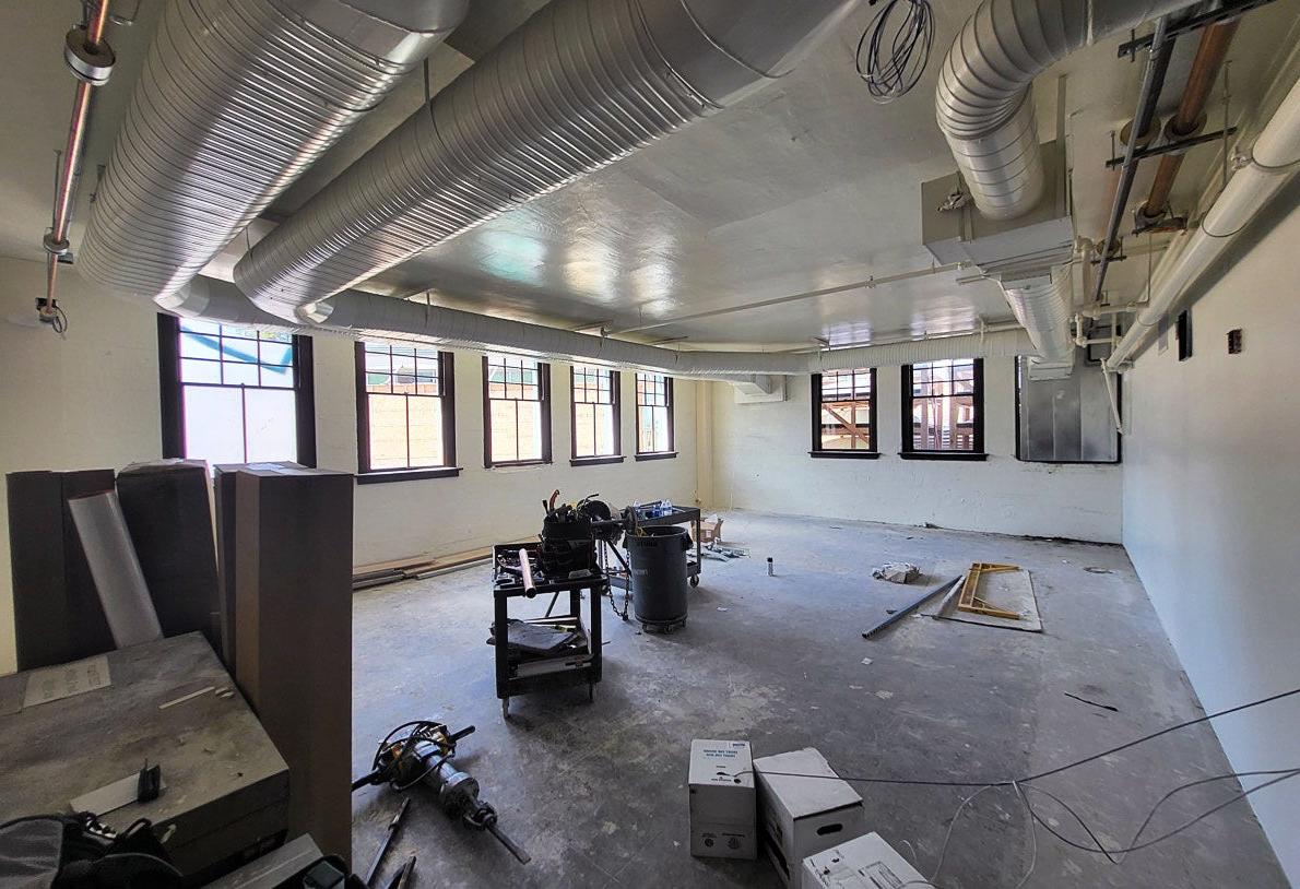 a room with windows on two walls has duct work in the ceiling. some equipment and construction tools are on the concrete floor