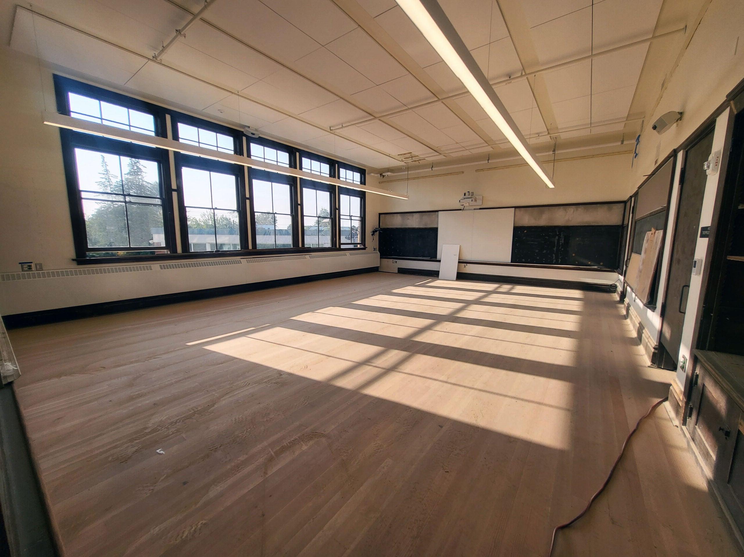 a classroom with a wood floor and wood framed windows